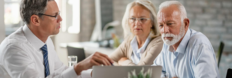A person is seen pointing a pen at the laptop screen while interacting with an elderly couple.
